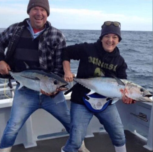 A man and a woman fishing on a boat, each holding a tuna fish