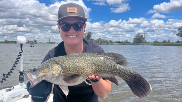 A person holding a Murray Cod fish on a boat with a lake in the background